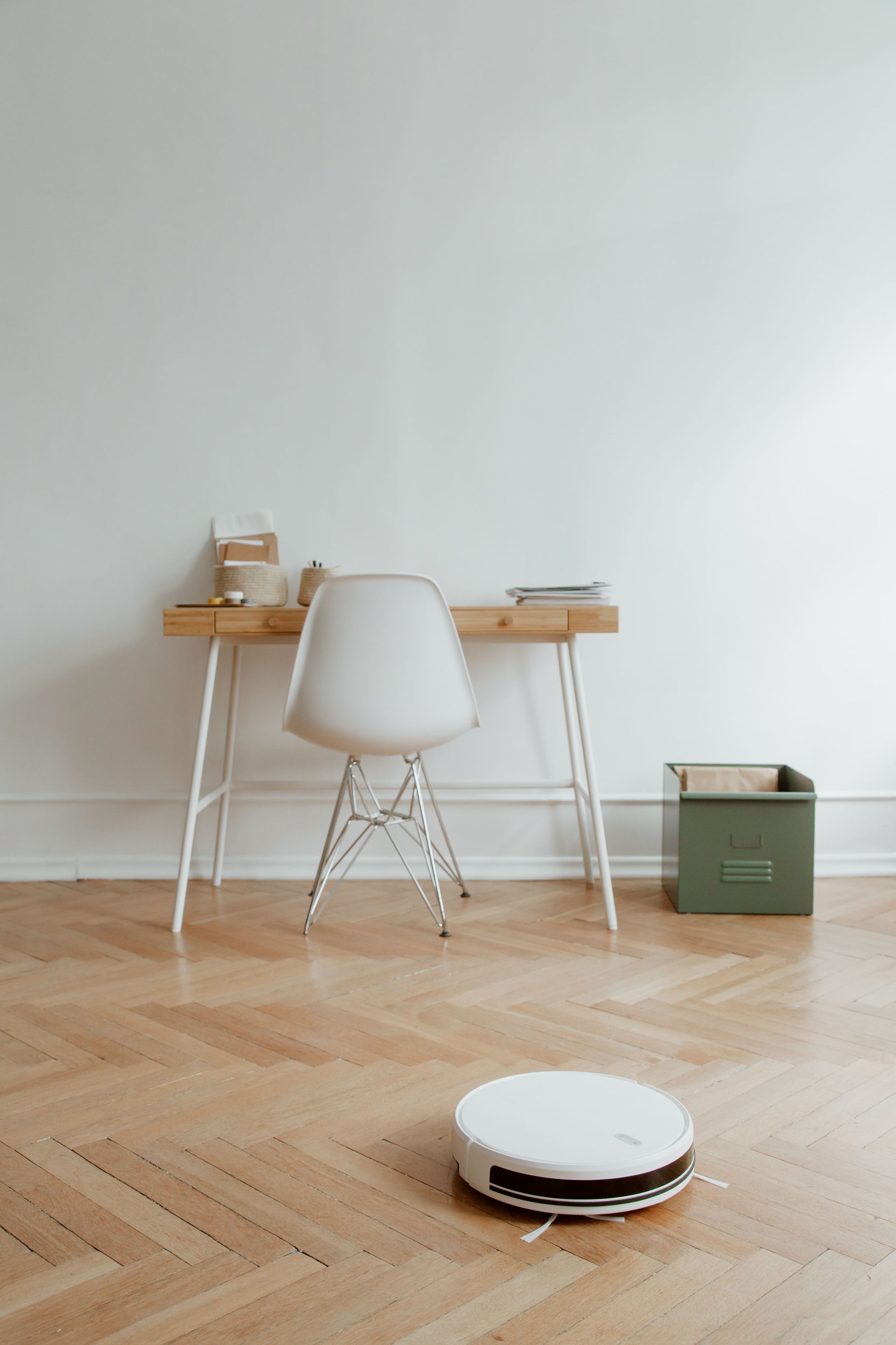 A sleek home office setup with a robot vacuum cleaning the wooden floor, emphasizing minimalism.